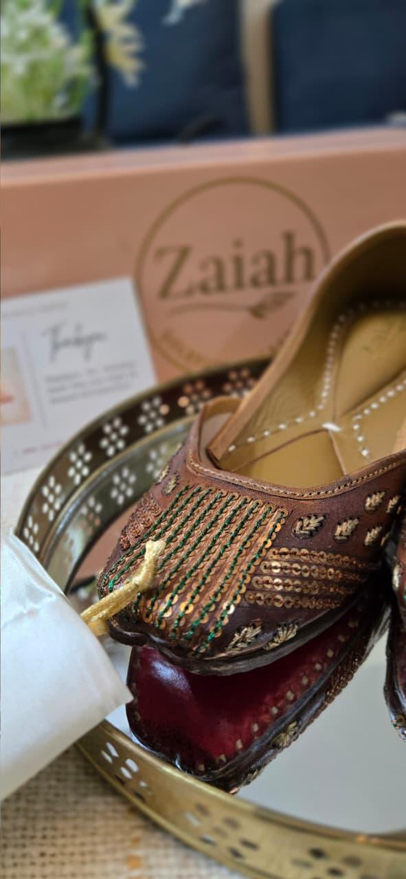 Decorative brinzebloom jutti with gold embellishments on a mirror with 'Zaiah' branding.