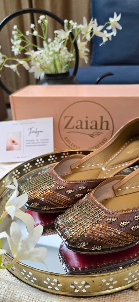 Decorative tray with bronzebloom jutti, a box labeled 'Zaiah', and flowers on a table.